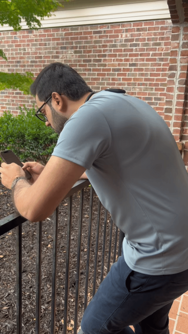 Man slouching while using smartphone outdoors, wearing R’LIEF smart posture corrector behind neck for discreet support